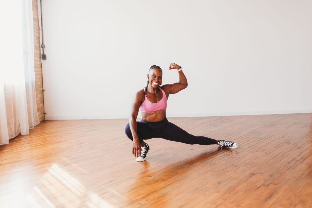Candace does a lunge while flexing her bicep and smiling